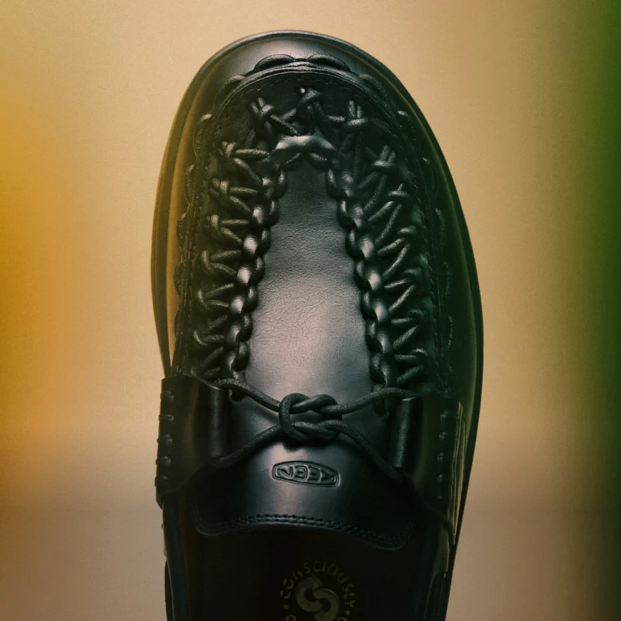 Closeup shot of the black leather Uneek loafer against a yellow and green gradient background.