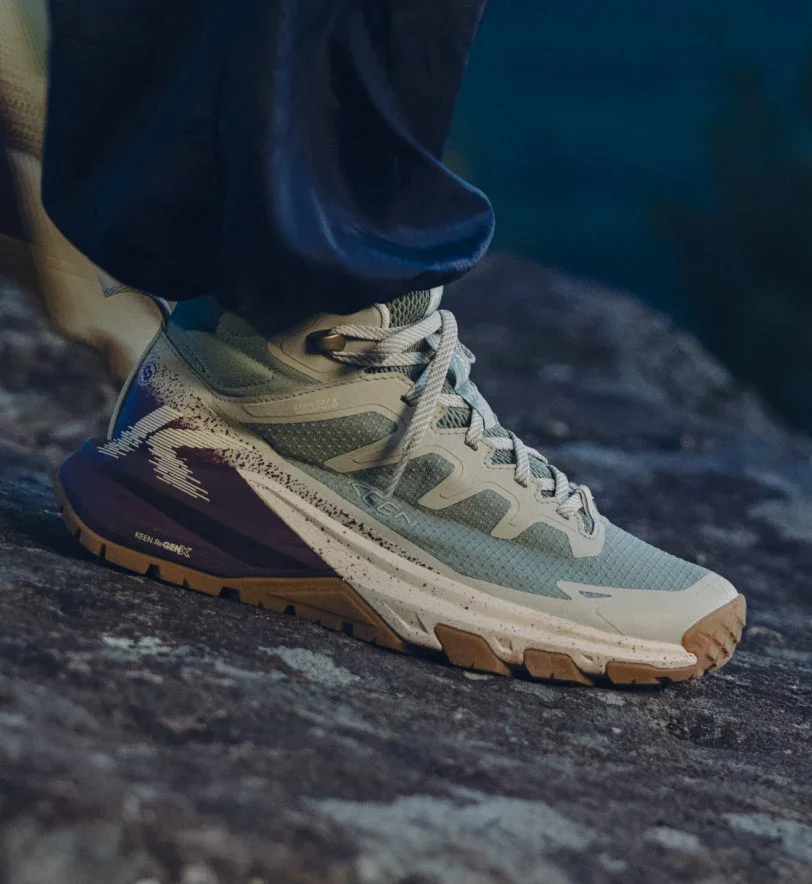 A woman stands on a rock, wearing Women's Targhee Apex boots and sneakers.