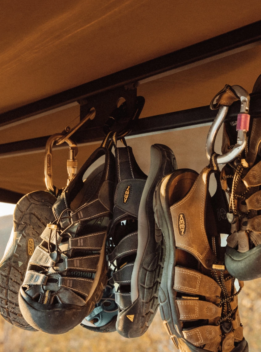 Three pairs of Newport sandals hanging from a van roof, attached with a carabiner